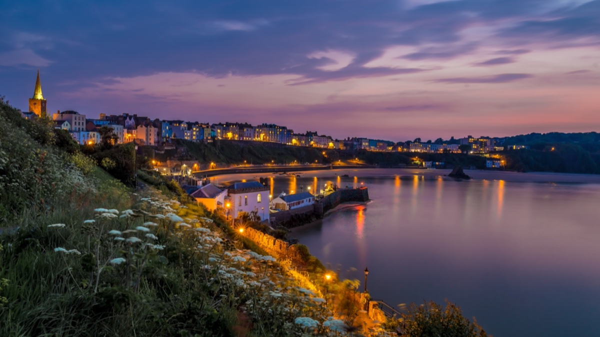 Tenby's lit harbour and seafront reflected in the bay after sunset
