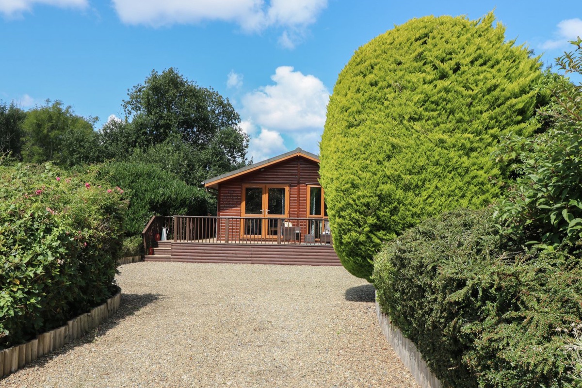 Timber lodge exterior framed by green hedges at 1 Hornbeam Lodge