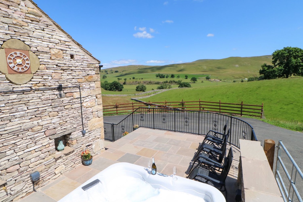 Hot tub beside stone barn walls with open fell views and a wall clock at Birkett Barn