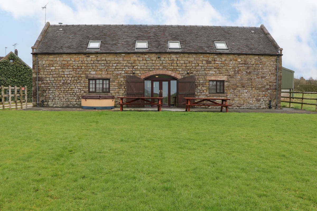 Large stone barn with a hot tub and picnic benches on the lawn at Bottomhouse Barn