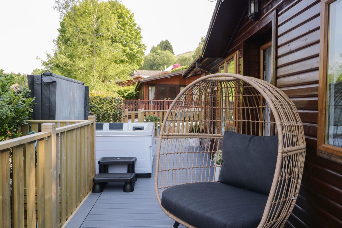 Timber deck with hanging rattan egg chair, hot tub, and woodland canopy above