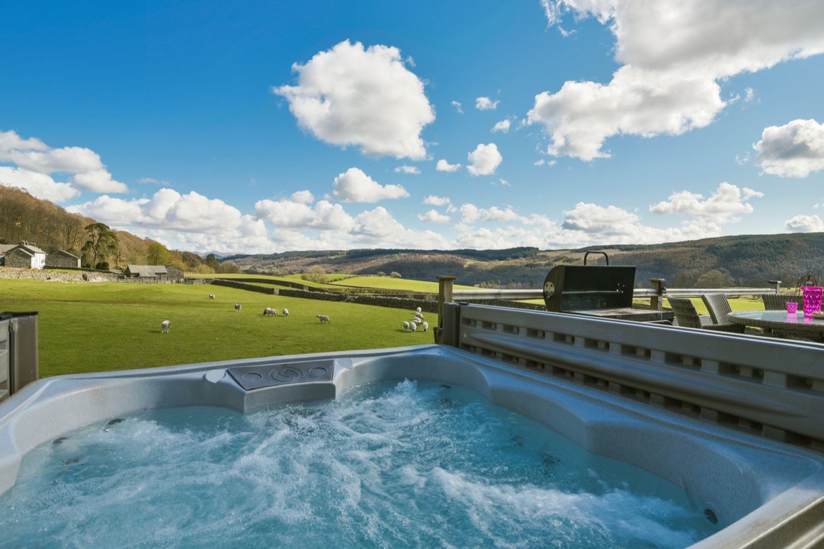 Hot tub on the raised deck with sheep grazing in green fell fields behind at Browside