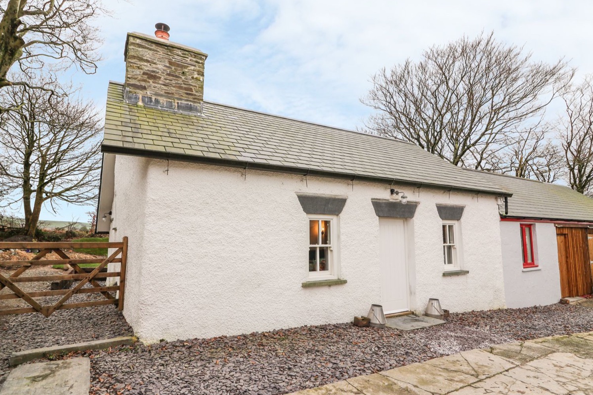 Whitewashed Welsh cottage with stone chimney and lit windows at Bwthyn Lan in Boncath