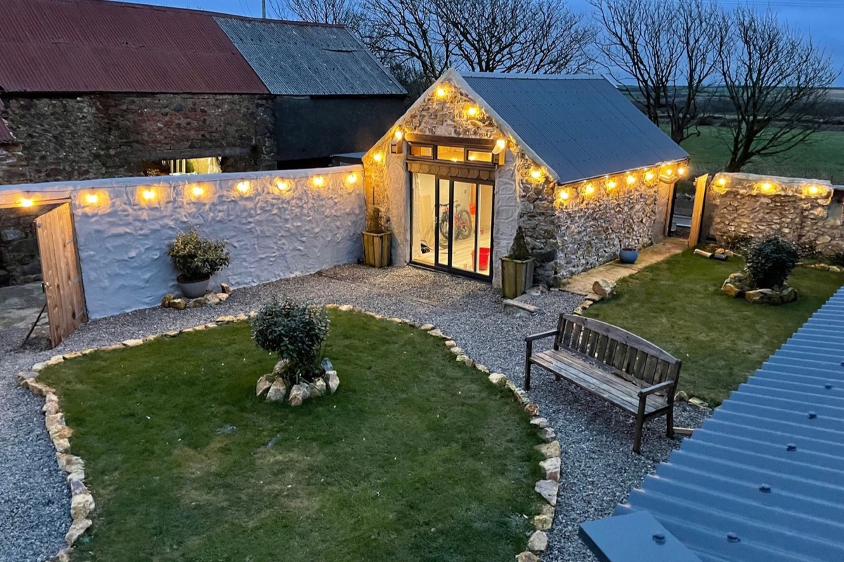 Clawddcam stone barn lit with festoon lights over a walled courtyard garden at dusk in Mathry