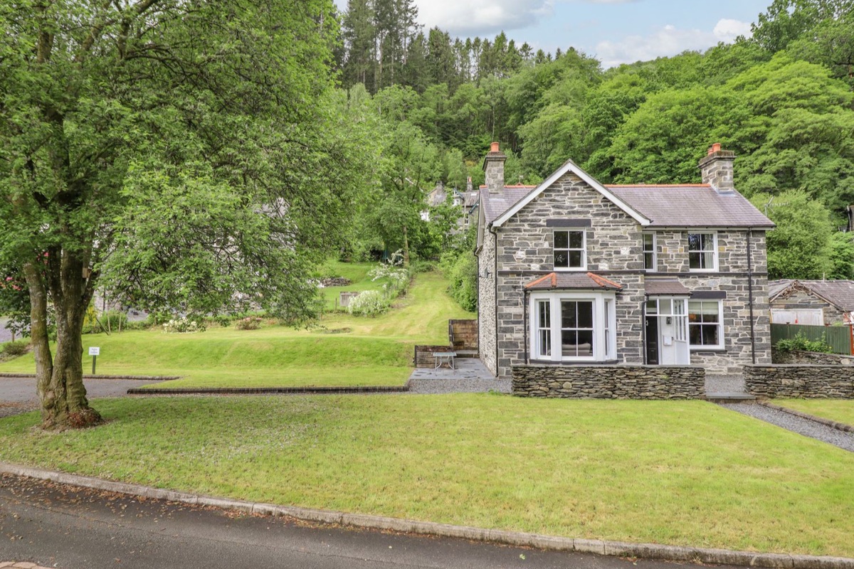 Craigside stone cottage exterior with lawn and wooded backdrop