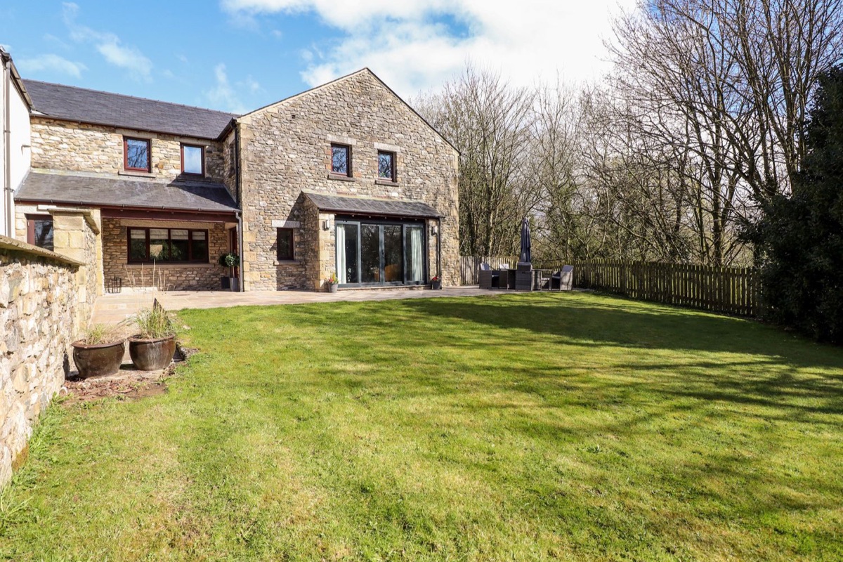 Stone cottage with modern glass extension and green lawn at Crooklands Cottage