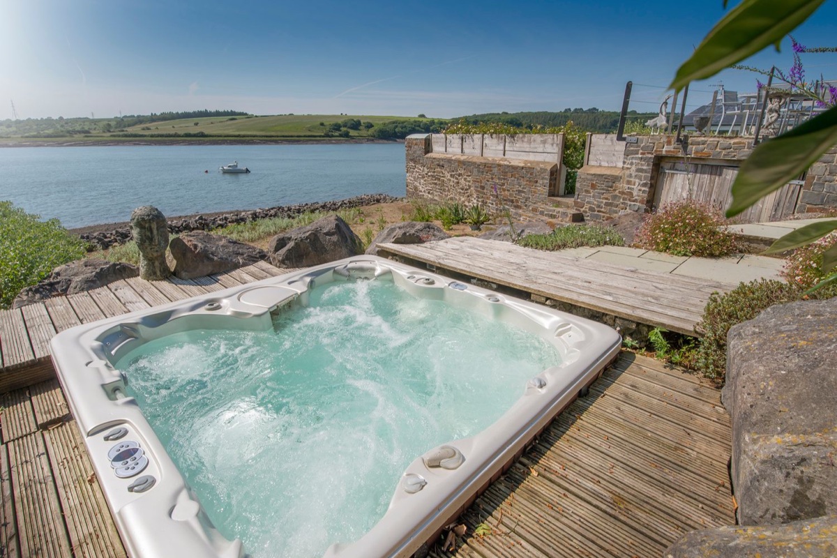 Hot tub beside the water with stone terraces at Curlew House