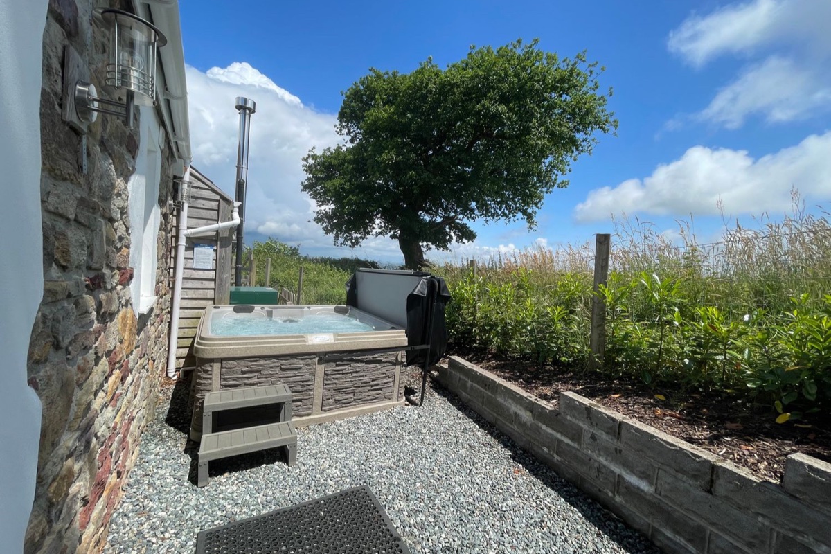 Hot tub beside the stone wall and oak tree at Dairy Cottage