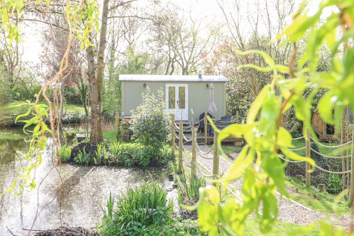 Damsel Shepherds Hut reflected in the water in a wooded garden