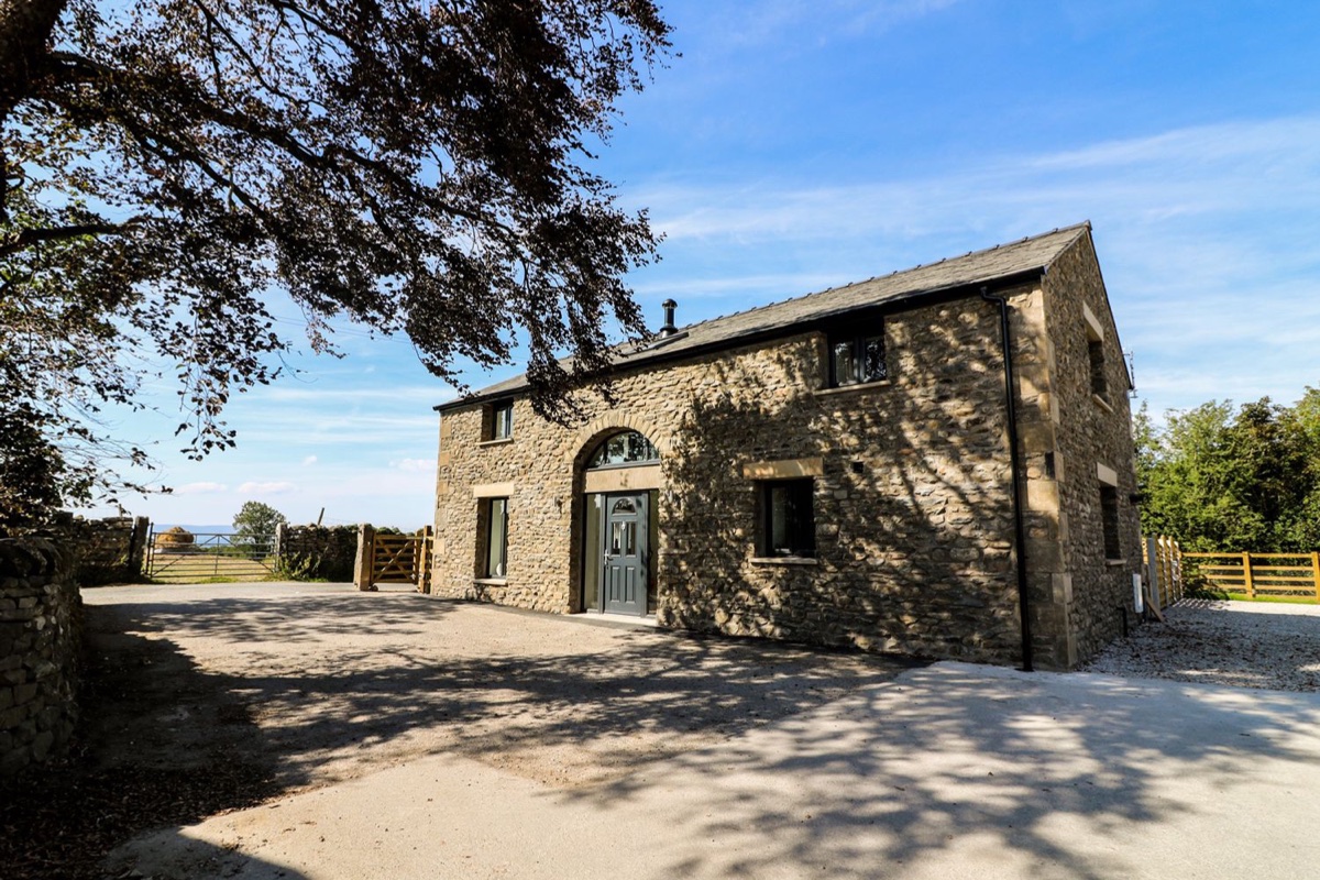 Stone barn exterior framed by trees under blue sky at Damson Barn near Kirkby Lonsdale