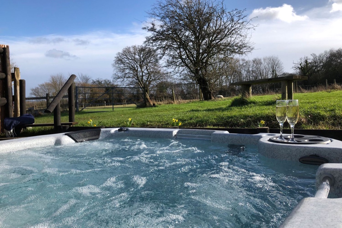 Hot tub at Deer Lodge, Wimborne Minster, with two filled champagne glasses and a field view beyond