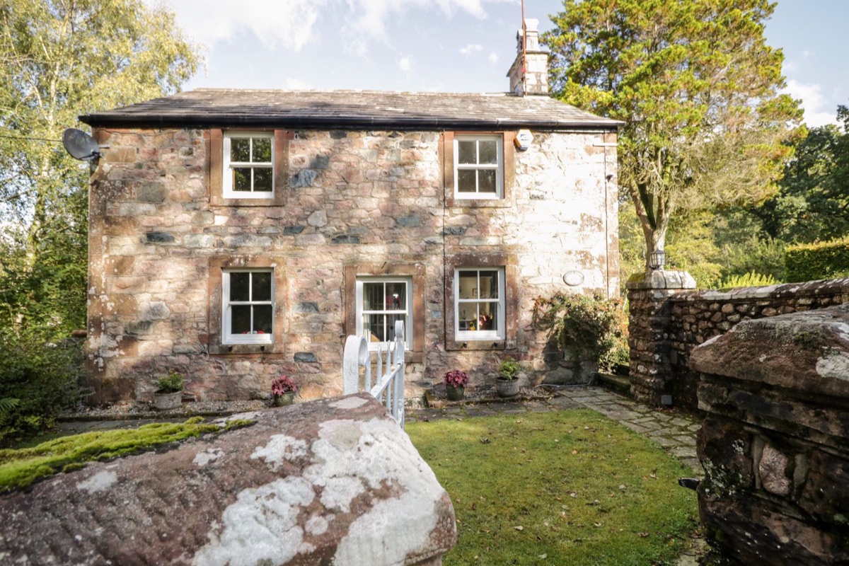 Red sandstone cottage with white windows set among a garden and mature trees at Fell Foot