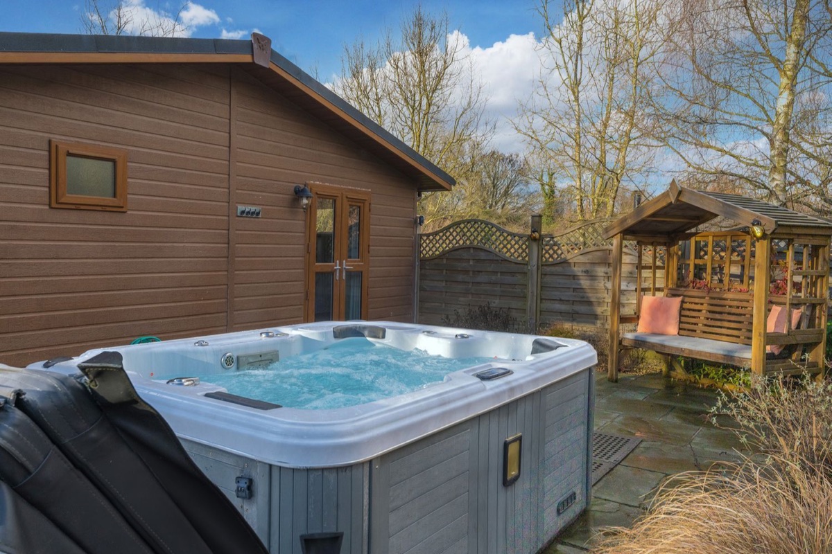 Hot tub beside the lodge with a wooden covered arbour and bench at Fern Lodge