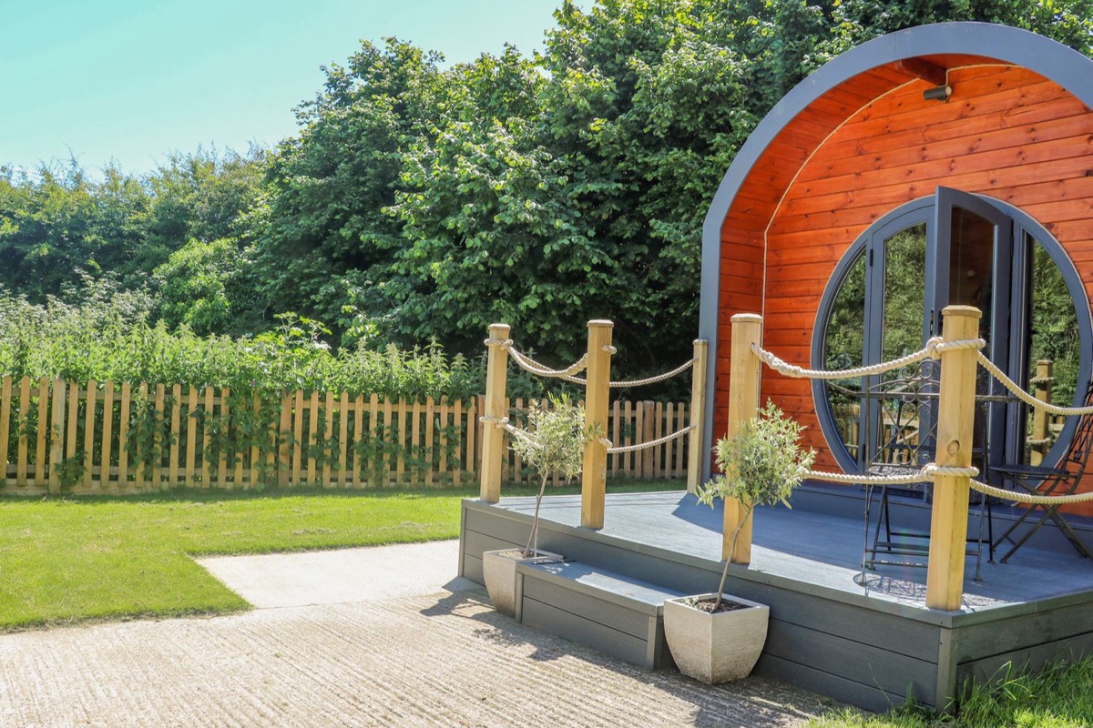 Filbert Pod, a curved timber glamping pod with a decked porch and bistro seating near Arundel