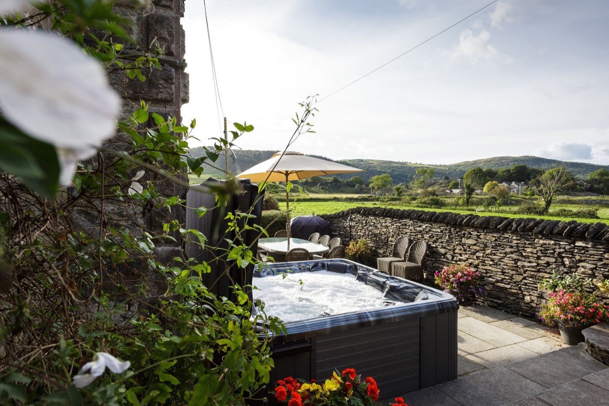 Hot tub framed by climbing roses with dry stone wall and Lakeland fells in the distance