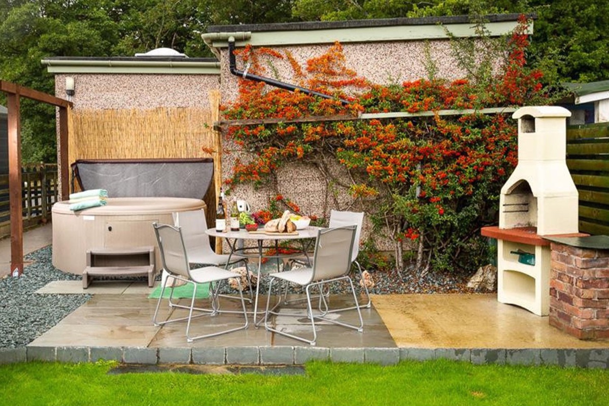 Round hot tub on the patio with a barbecue grill and pyracantha bush against cream-rendered walls