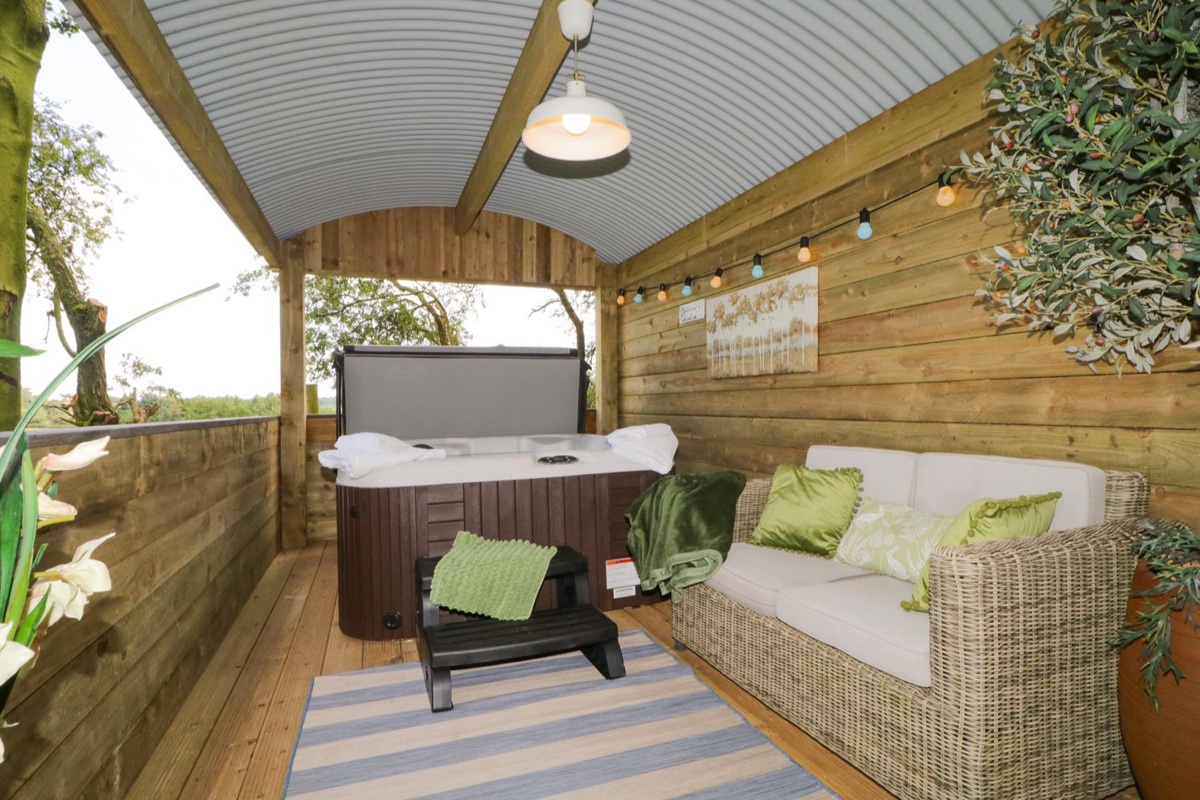 Covered hot tub shelter with sofa and string lights at High Rigg Shepherd's Sunset