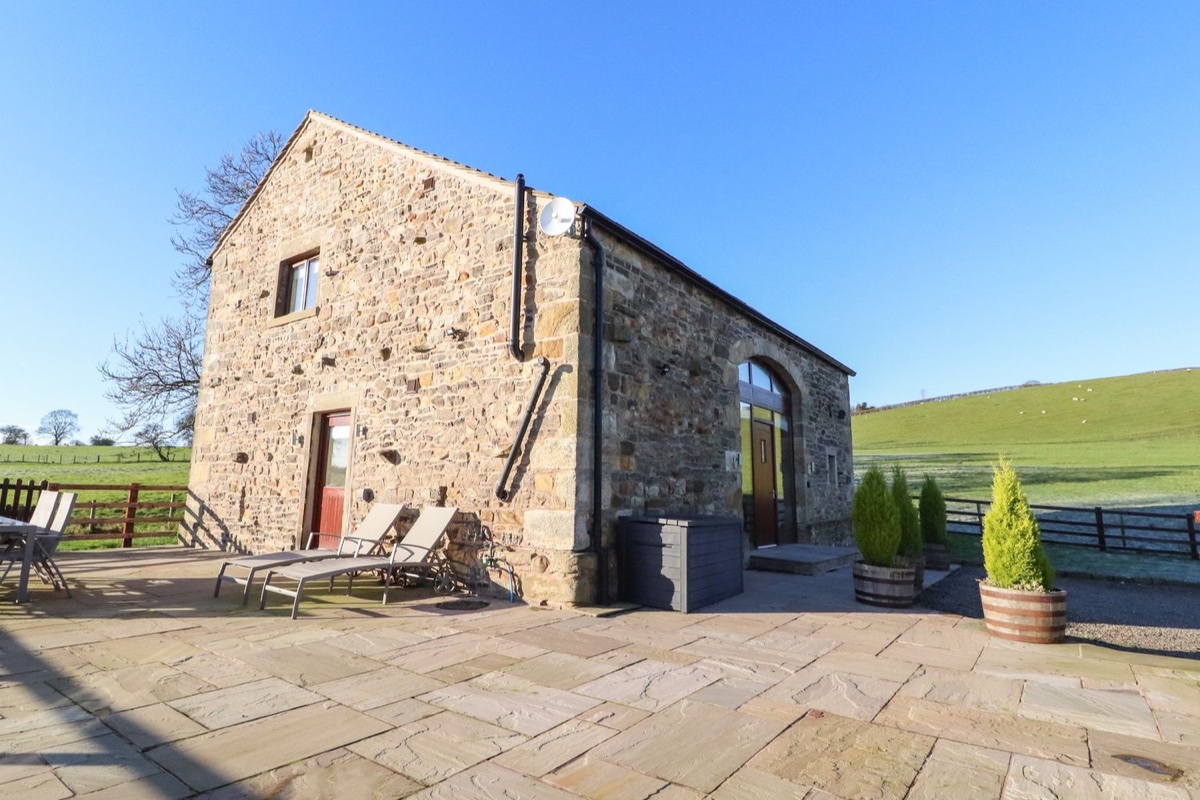 Hill Brook Barn stone exterior with patio chairs and open fields