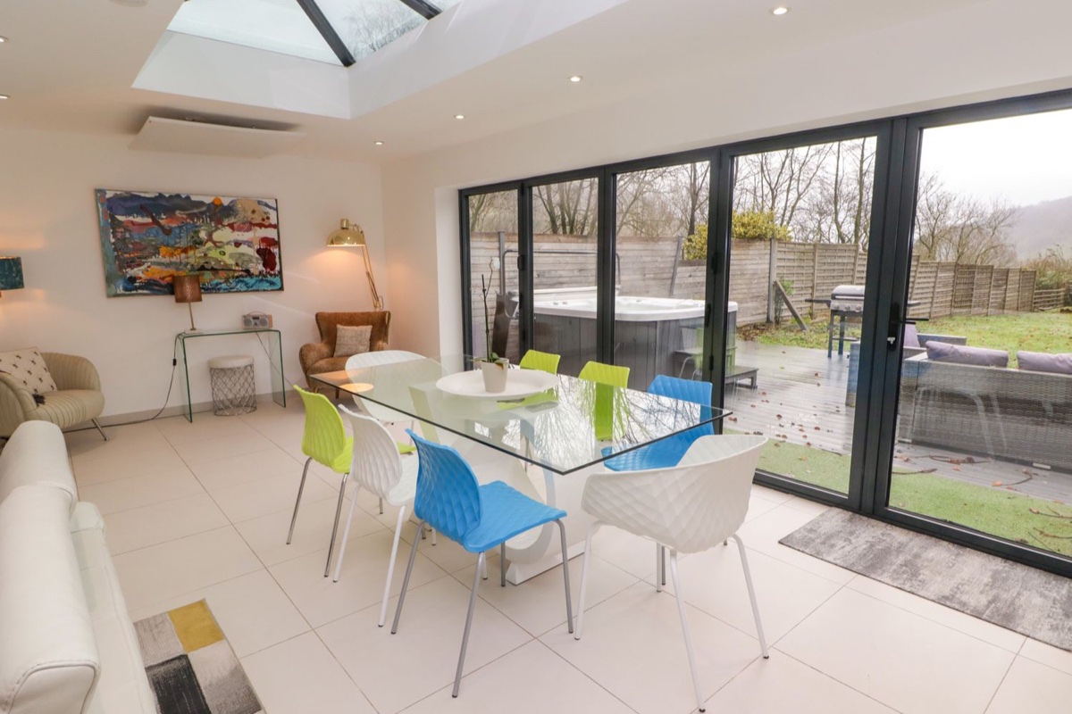 Bright dining room with skylight, colourful chairs and bifold doors to the garden at Hiraeth