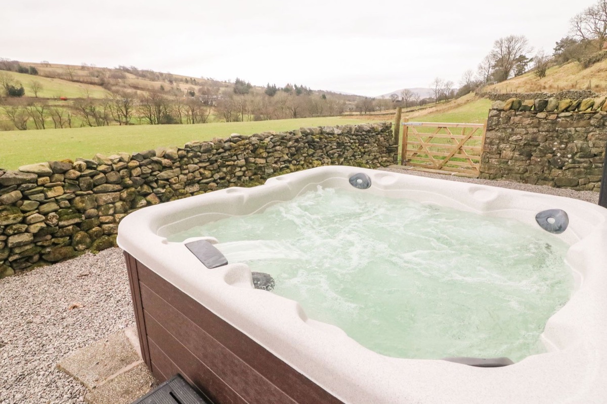 Bubbling hot tub beside a dry stone wall with a five-bar gate and green rolling hills beyond