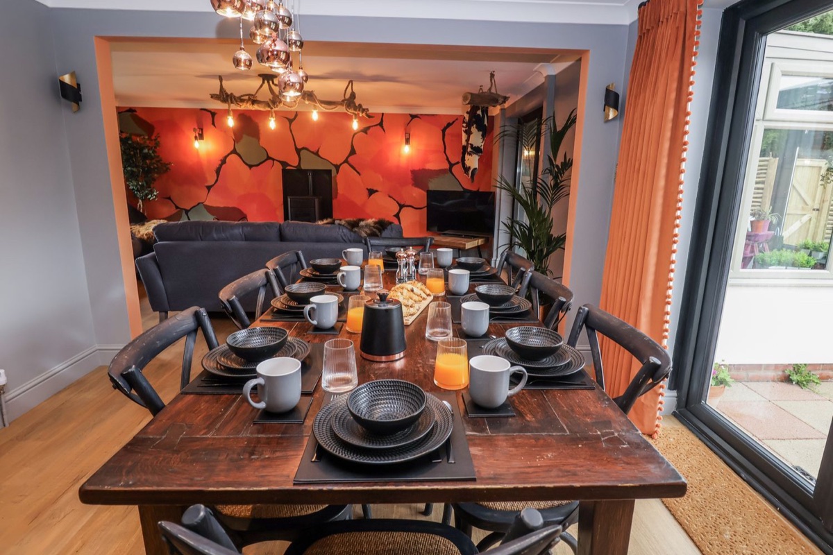 Dining table set in front of a bold orange-walled lounge at Holly Farm and Annexe
