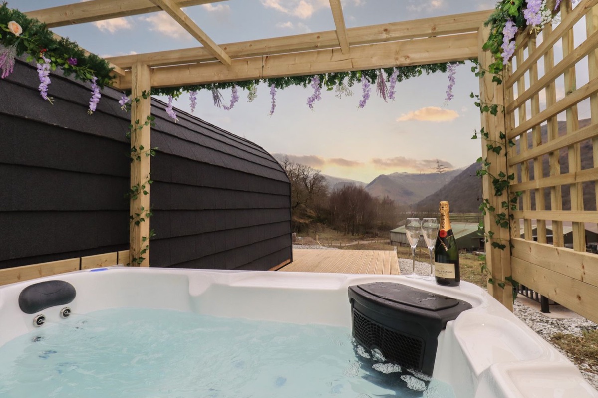 Hot tub with champagne under a wisteria-draped pergola framing mountain fell and valley views