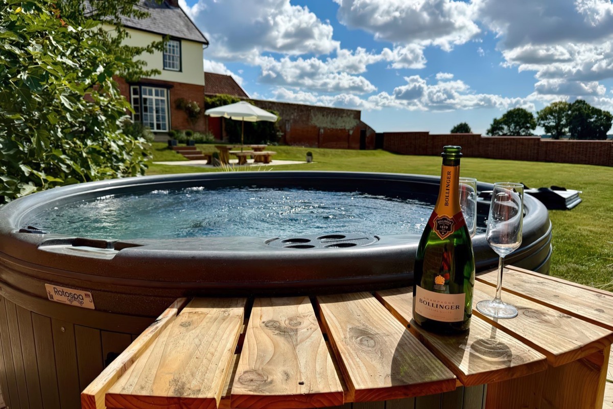 Wood-fired hot tub with the house and garden beyond at Knights Farm