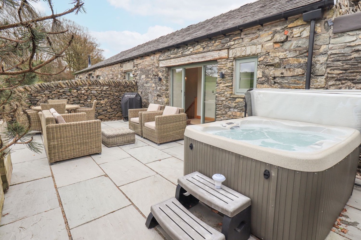 Hot tub on a stone patio with wicker chairs beside the barn at Lime Cottage