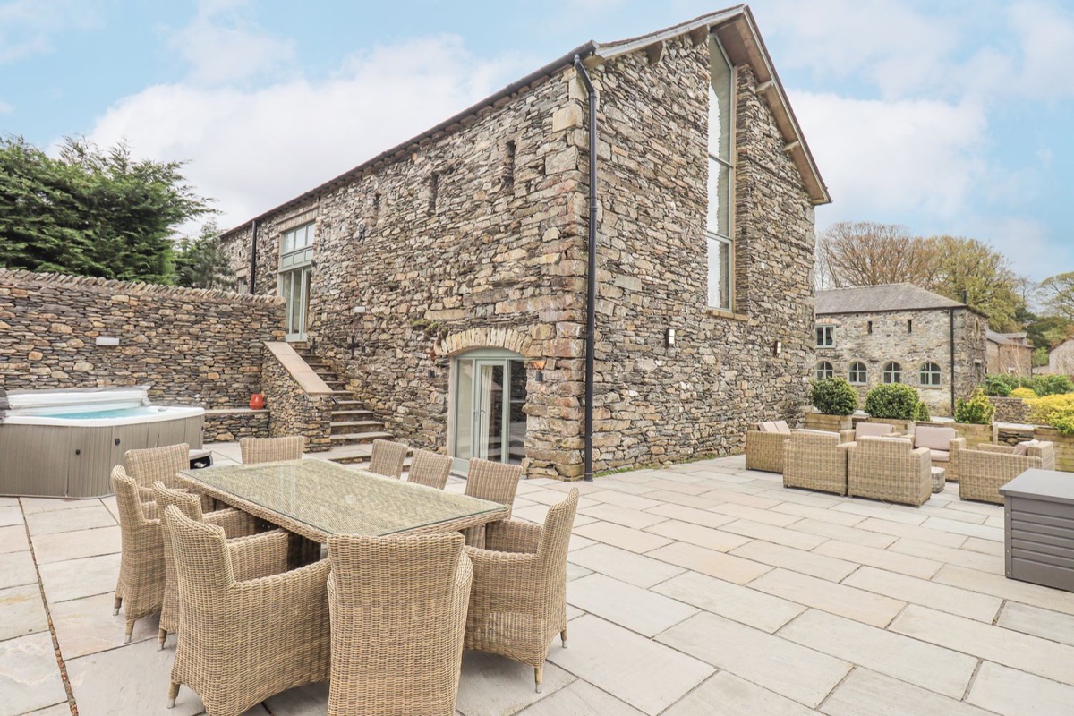 Stone barn patio with a wicker dining table set for four and hot tub at Oak Cottage