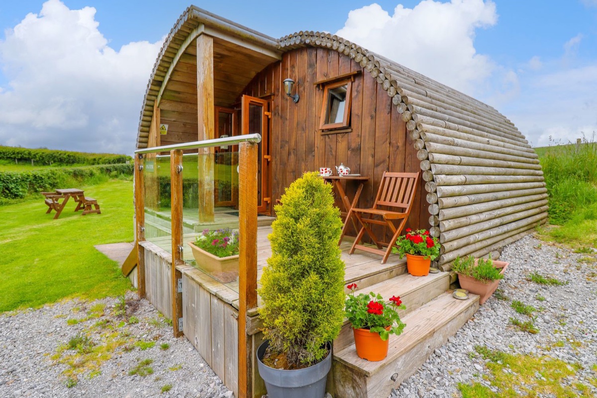 Wooden glamping pod with glass-railed porch and potted plants at Oak View