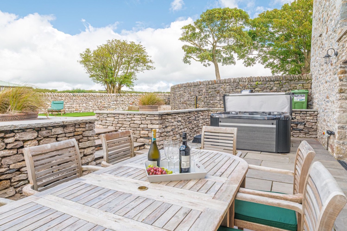 Stone-walled patio with dining table, wine, and hot tub at The Old Stable