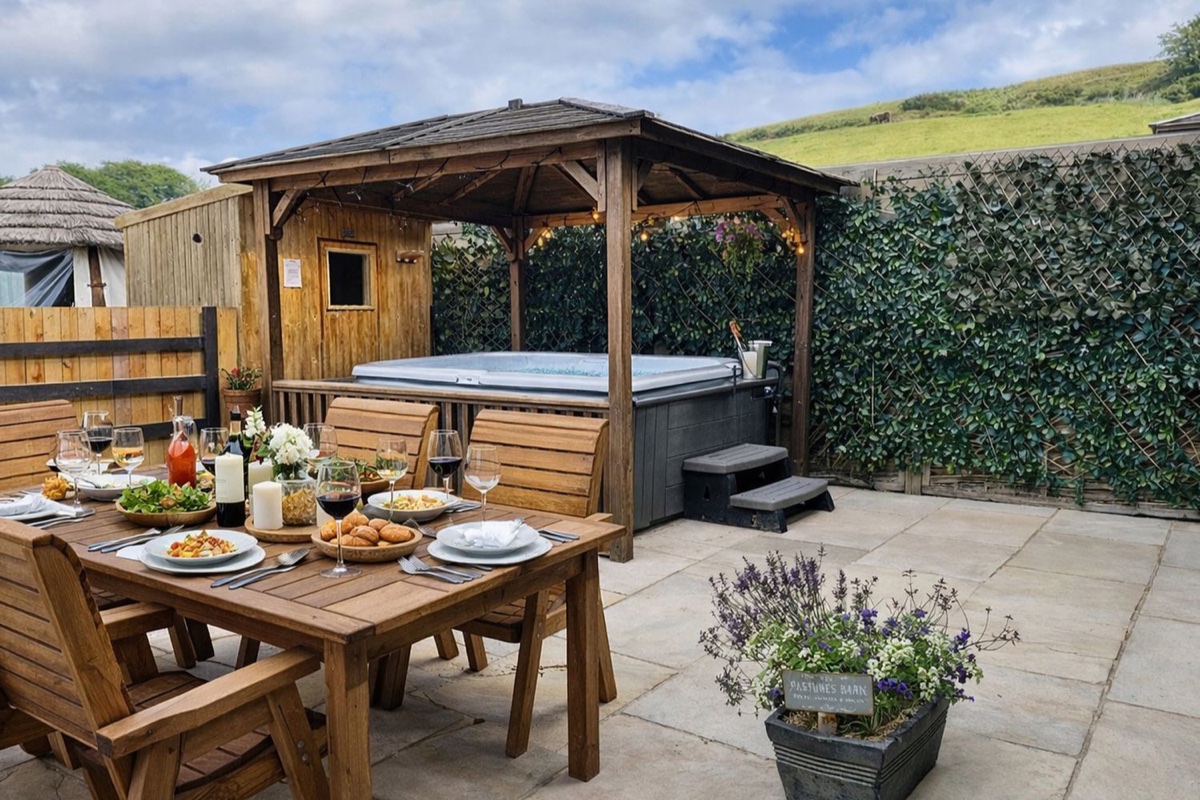 Hot tub under a gazebo beside an outdoor dining table with hillside views at Pastures Barn