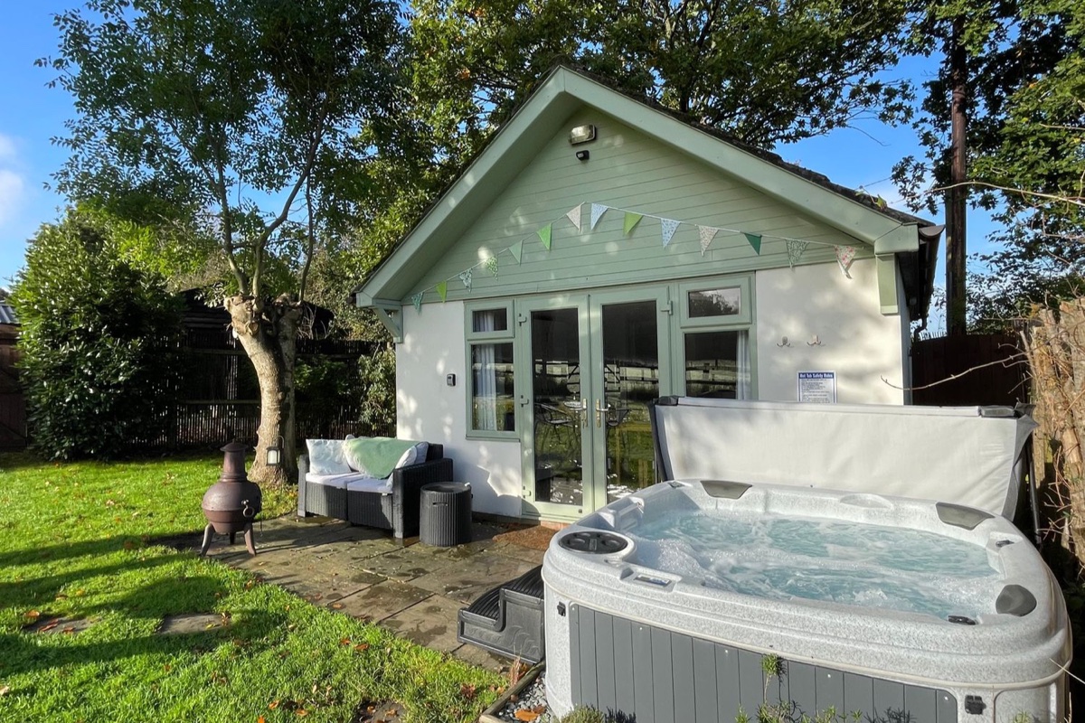 Sage-green Pheasant Lodge near Wimborne Minster with bunting, a hot tub and garden seating in the sun