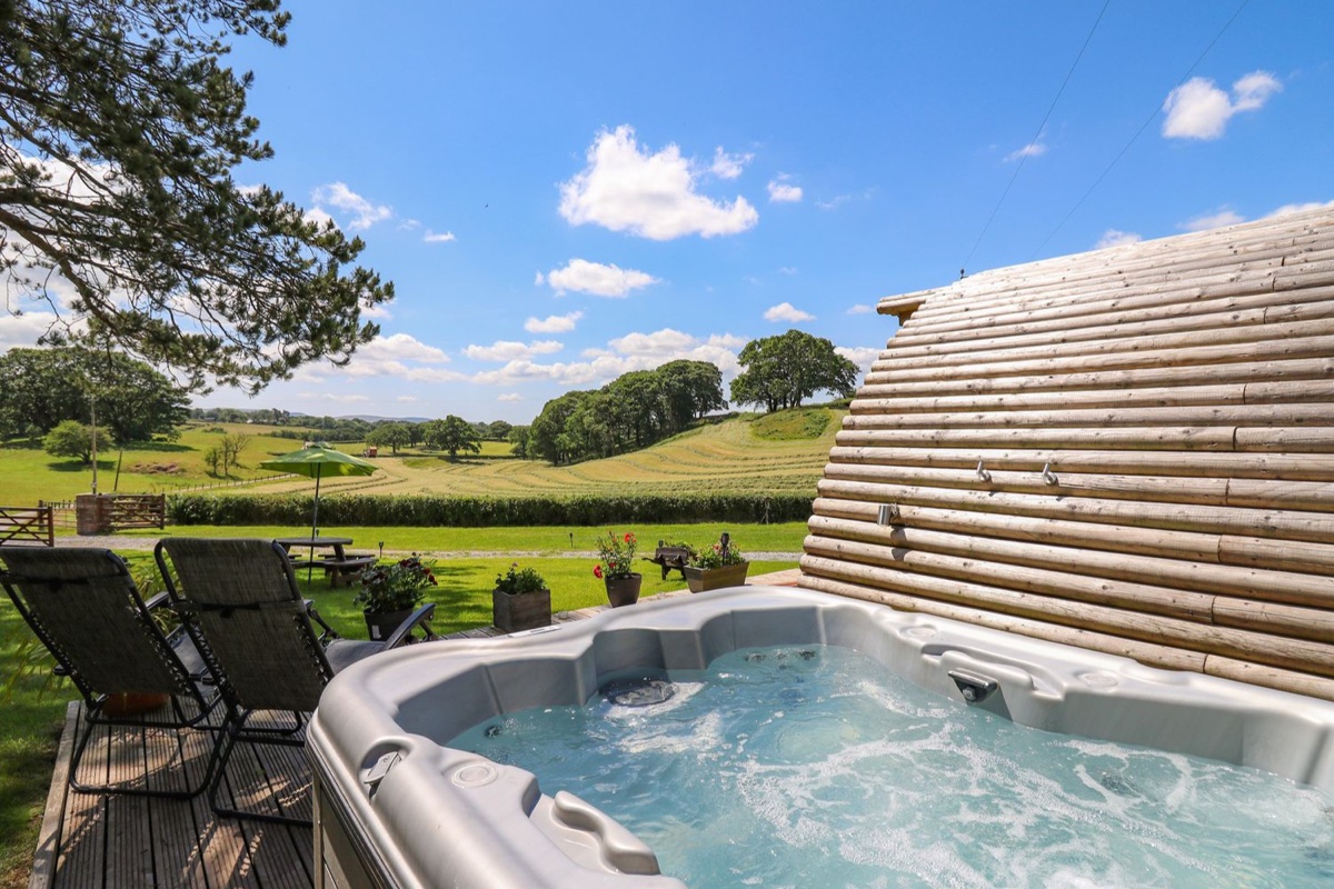 Hot tub with sun loungers overlooking rolling green countryside at Pine Lodge