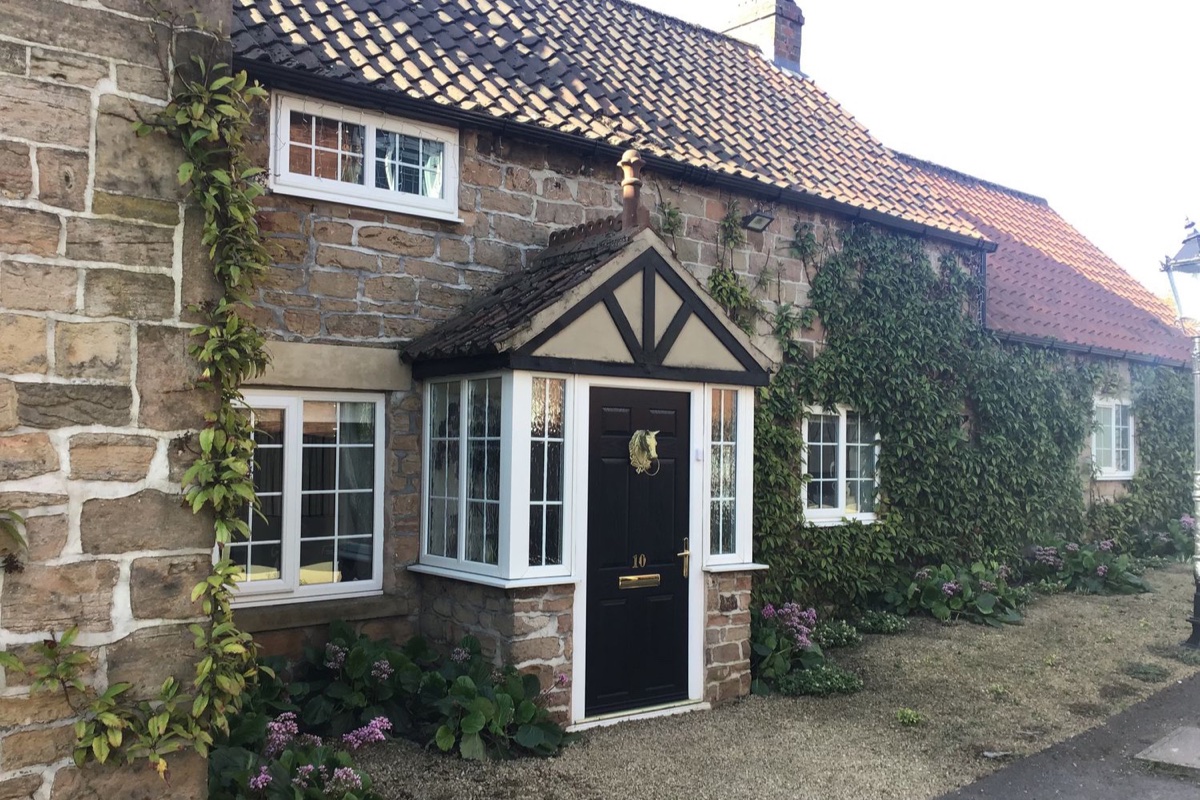 Rose Cottage stone frontage with black door and climbing greenery