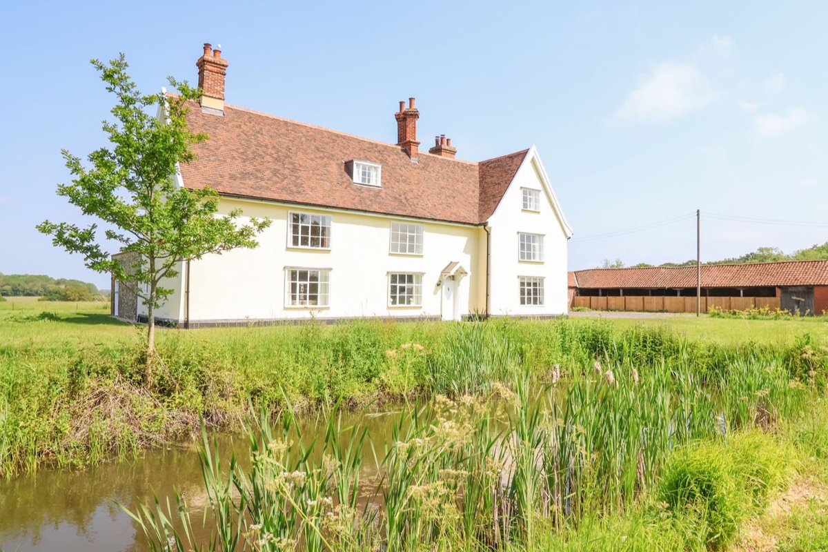 South Grange House across a pond with lawns and Suffolk countryside
