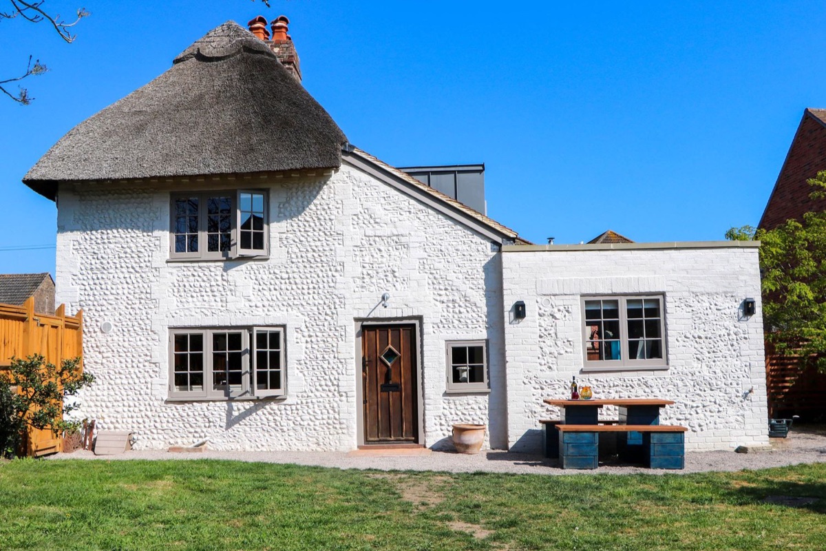 Spring Cottage, a white thatched cottage with a wooden door and lawn near Arundel