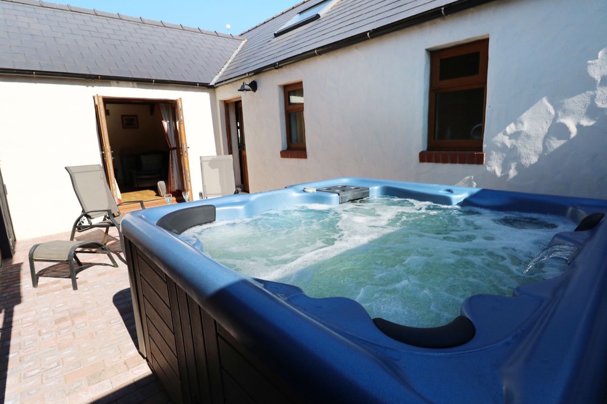Courtyard hot tub at Stable Cottage with the stone stable building and open doors behind