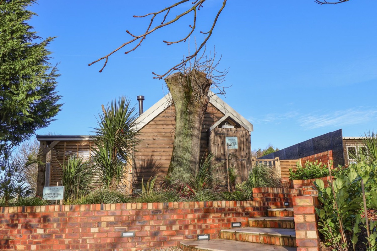 Sunset Retreat timber cabin exterior behind brick steps and planting