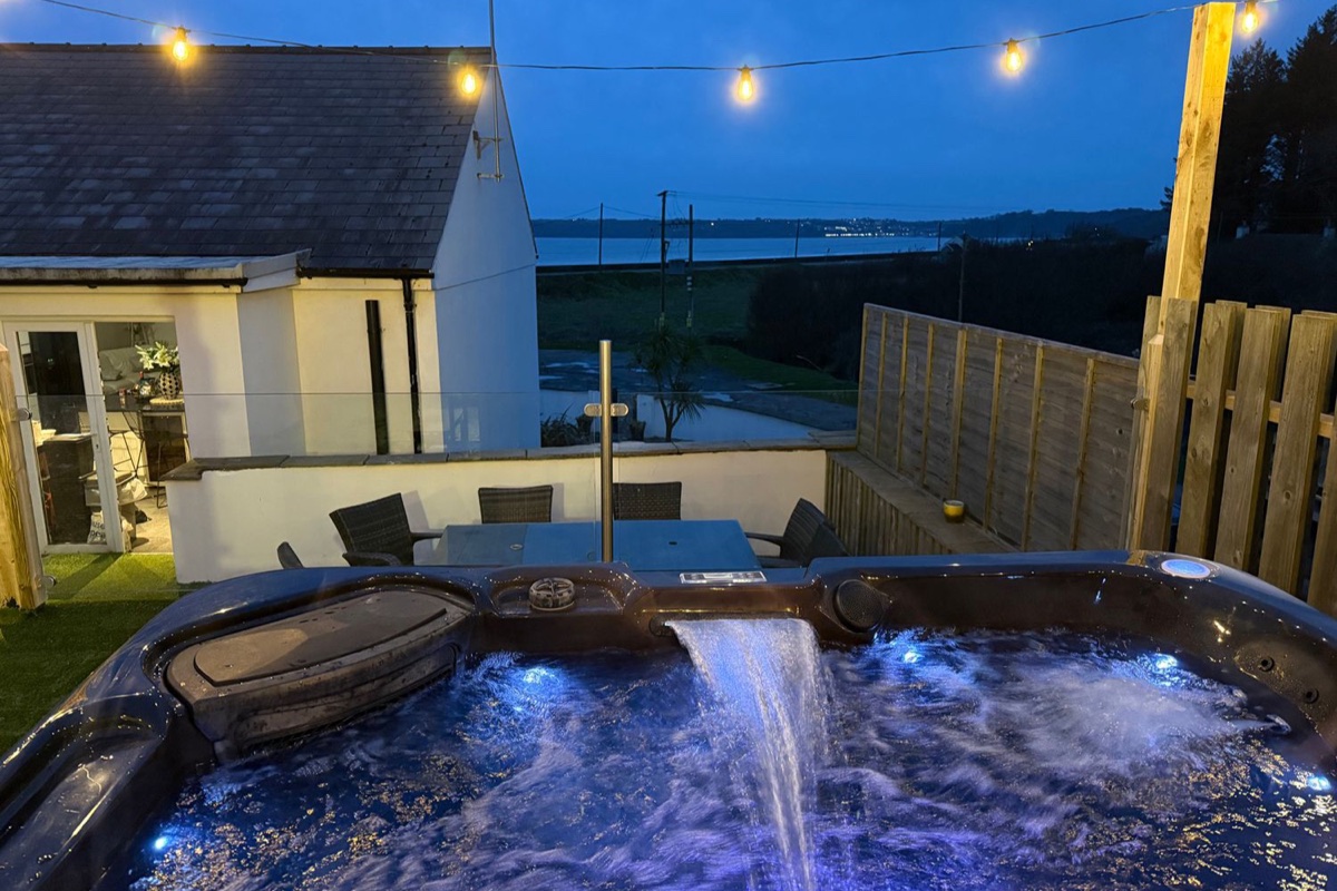 Hot tub under evening lights with the house beyond at Swn y mor