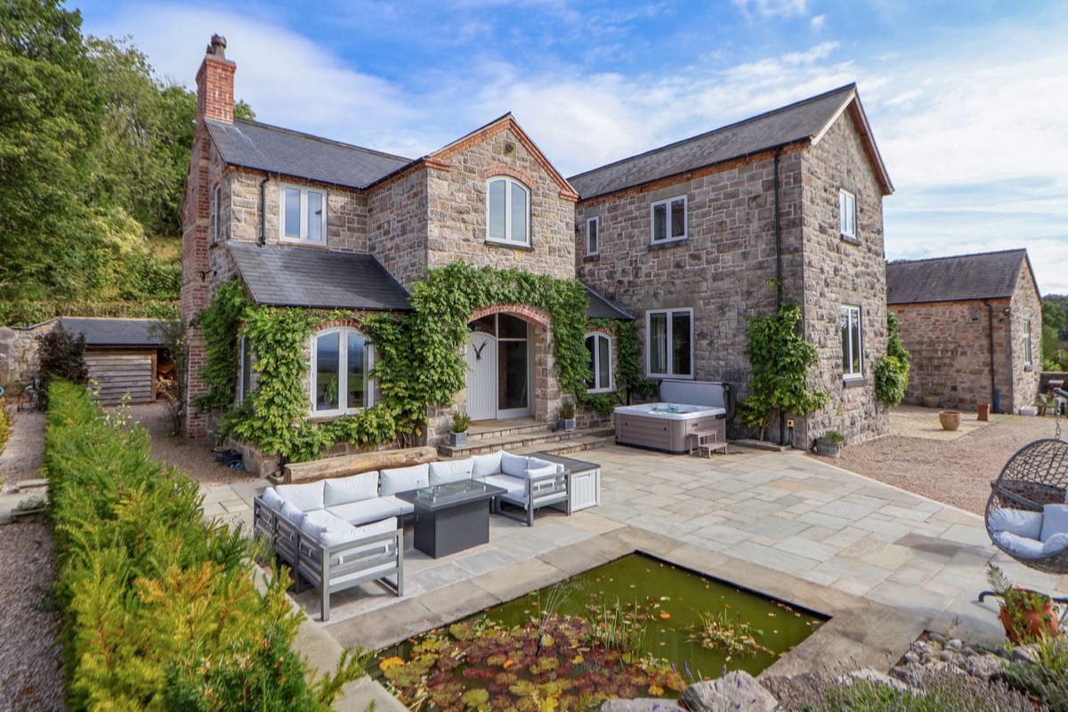 Tanat House stone exterior with patio seating, pond and hot tub
