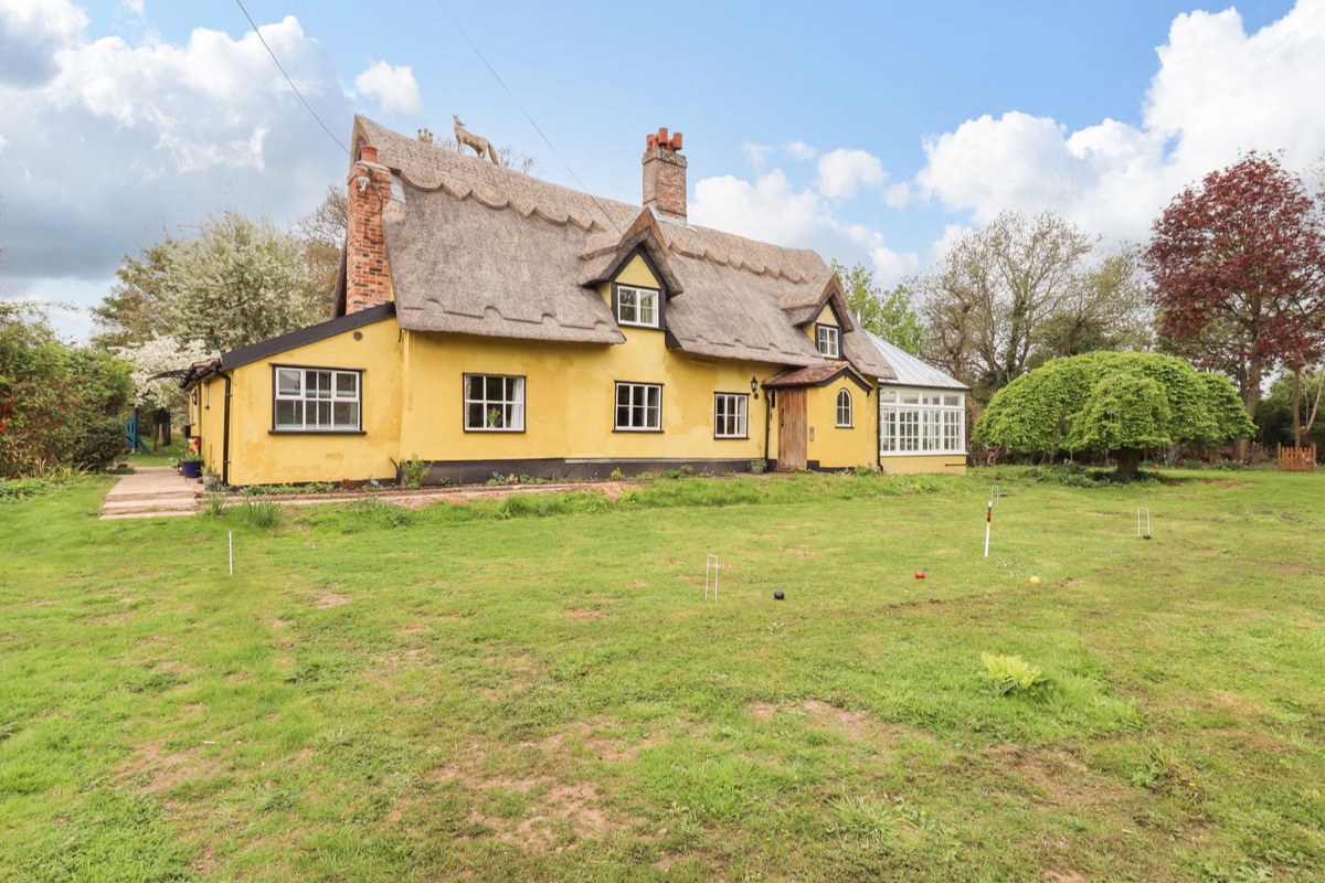 Yellow thatched Abbey Cottage with a garden lawn
