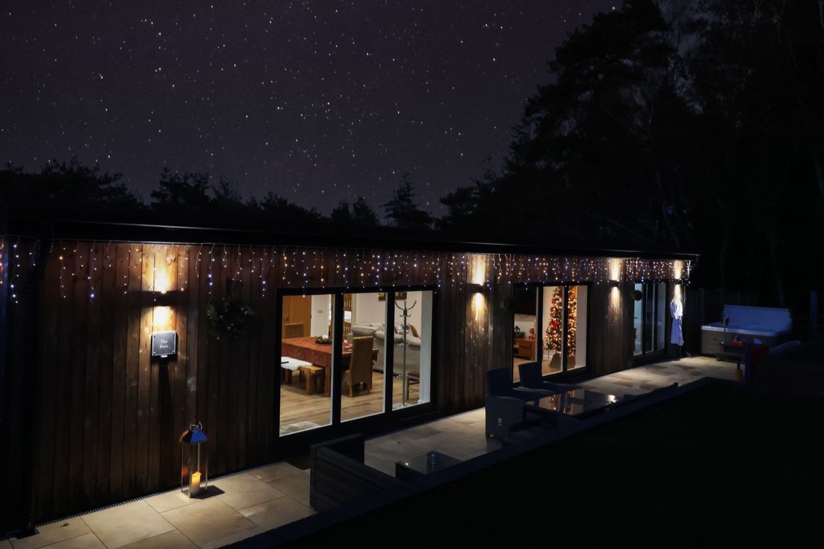 Single-storey timber barn at Lytchett Matravers at night under a starfield, fairy lights along the eaves and lit windows