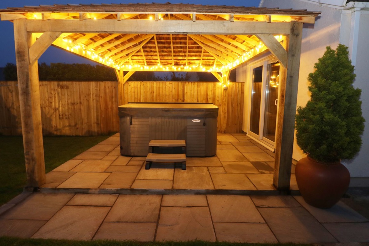 Hot tub under a lit wooden gazebo at dusk at The Elms in Milford Haven