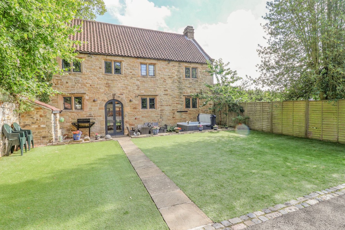 The Gatehouse stone exterior with lawn and hot tub in an enclosed garden