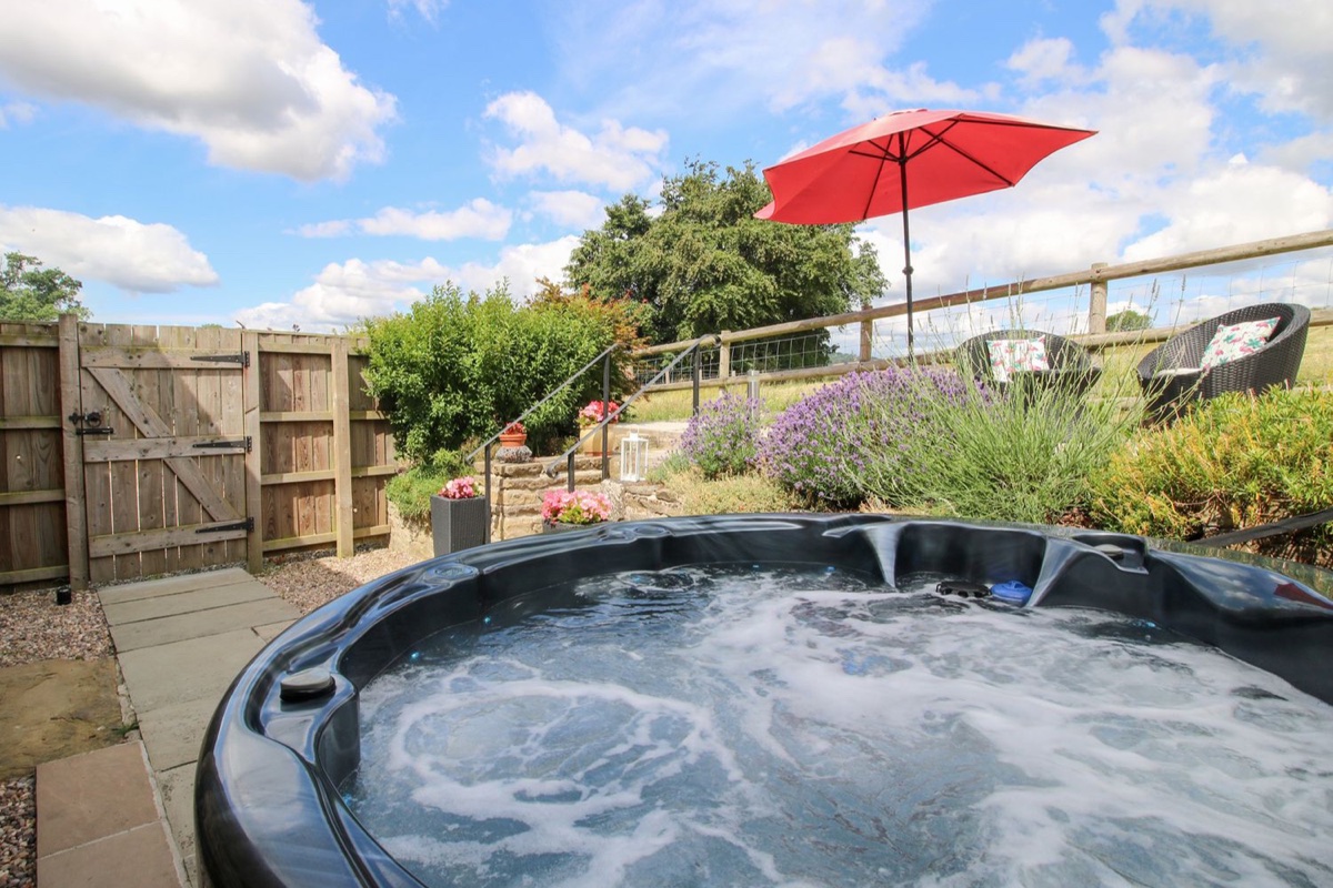 Hot tub at The Hay Loft with red parasol and countryside views