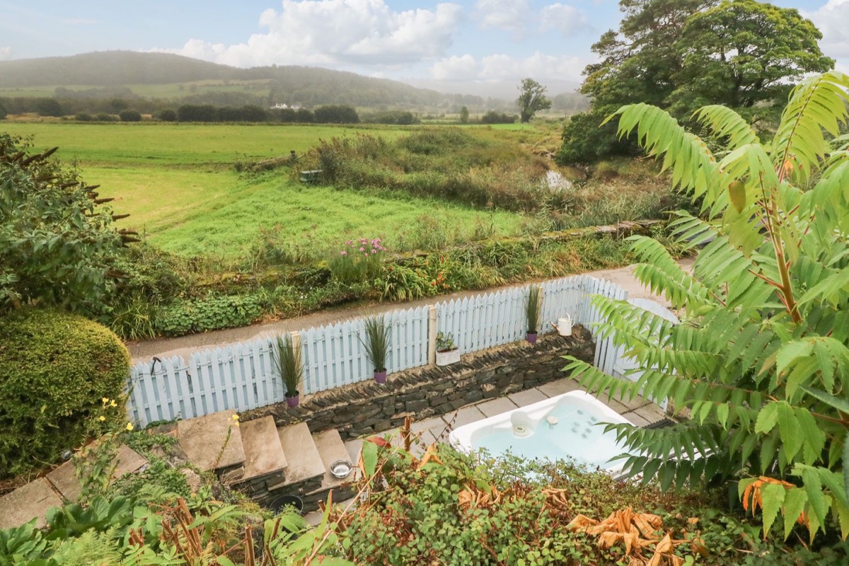Hot tub viewed from above through foliage with green fields beyond at The Lodge