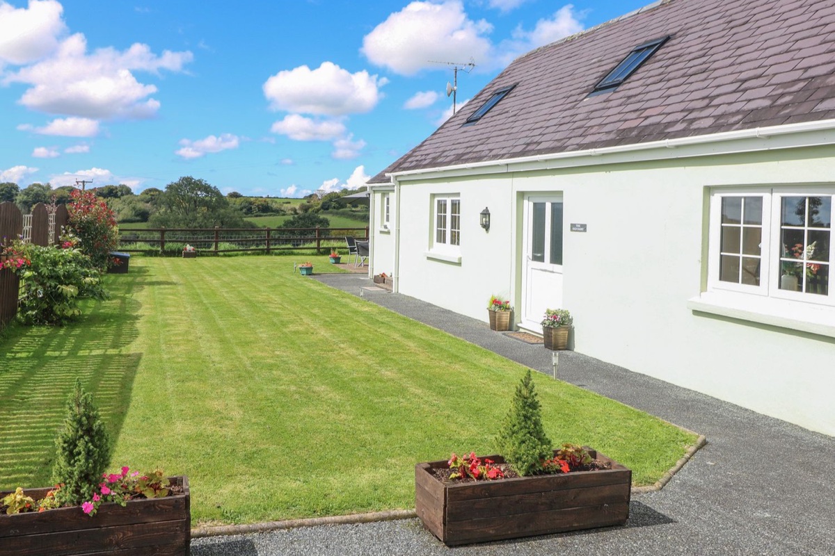 Green-rendered single-storey cottage with a striped lawn at The Old Dairy