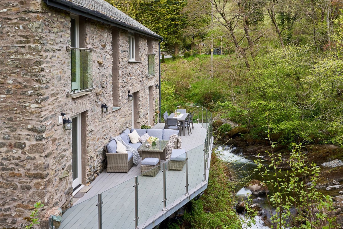 Timber deck cantilevered over a stream with potted plants at The Old Water Mill
