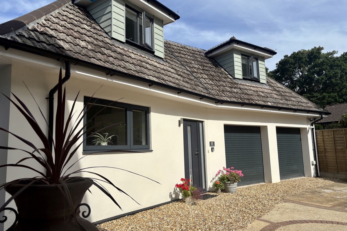 White rendered cottage with dormer windows, grey garage doors and gravel drive at The Retreat, Ferndown